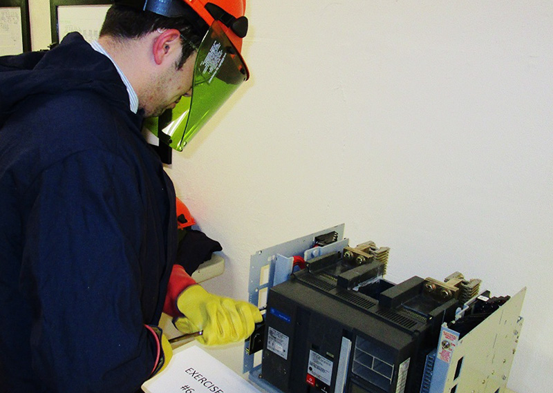 Students will also learn and practice skills on real, but de-energized equipment. This allows students to focus on proper technique without the hazards present.  Here a student learns how to rack in and out a breaker while wearing proper PPE.  